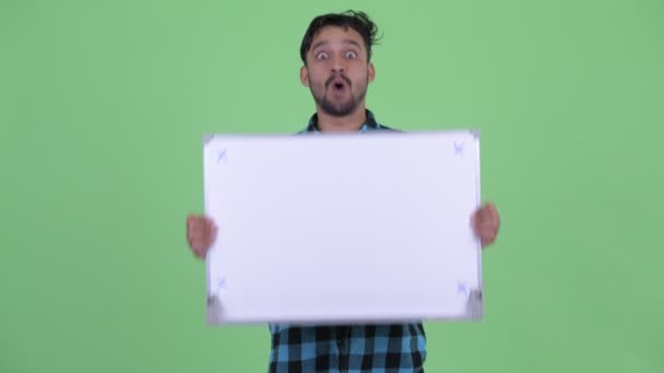 Glückliche junge bärtige persische Hipster-Mann hält Whiteboard und sieht überrascht — Stockvideo