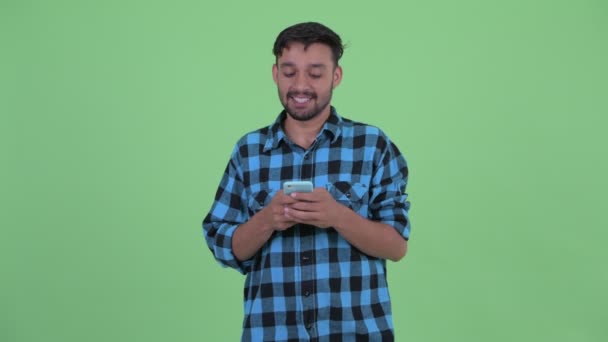 Happy young bearded Persian hipster man thinking while using phone — Stok Video