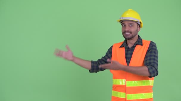 Feliz joven barbudo hombre persa trabajador de la construcción mostrando algo y mirando emocionado — Vídeos de Stock