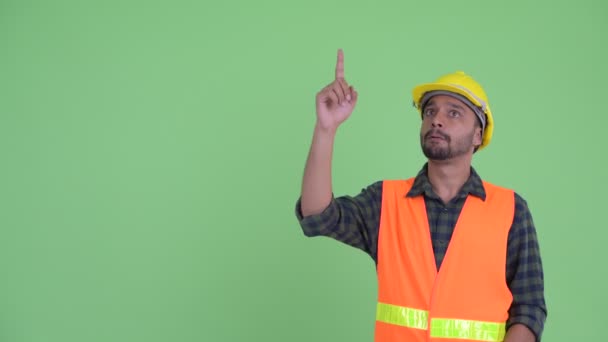Joven barbudo hombre persa trabajador de la construcción pensando mientras señala hacia arriba — Vídeos de Stock