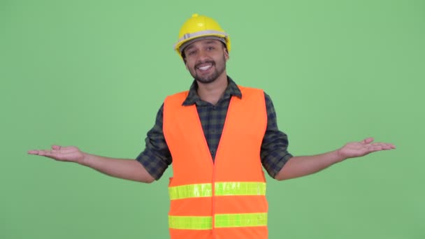 Gelukkige jonge bebaarde Perzische man bouwvakker die iets vergelijkt — Stockvideo