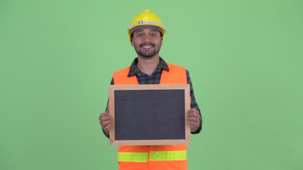 Feliz joven barbudo persa trabajador de la construcción hablando mientras sostiene pizarra — Vídeos de Stock