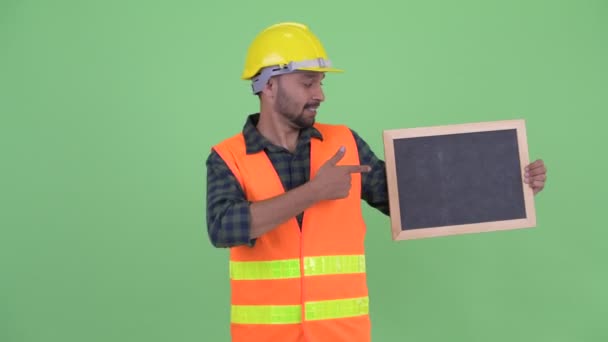 Happy young bearded Persian man construction worker holding blackboard and giving thumbs up — Stock Video