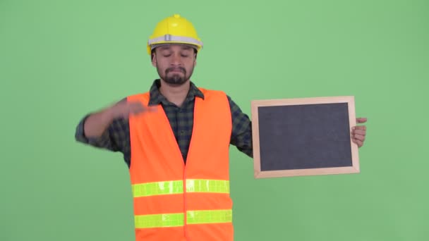 Stressed young bearded Persian man construction worker holding blackboard and giving thumbs down — Stock Video