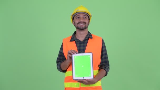 Feliz joven barbudo hombre persa trabajador de la construcción pensando mientras muestra tableta digital — Vídeo de stock