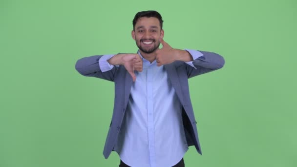 Счастливый молодой бородатый персидский бизнесмен выбирает между большим и большим пальцами вниз — стоковое видео