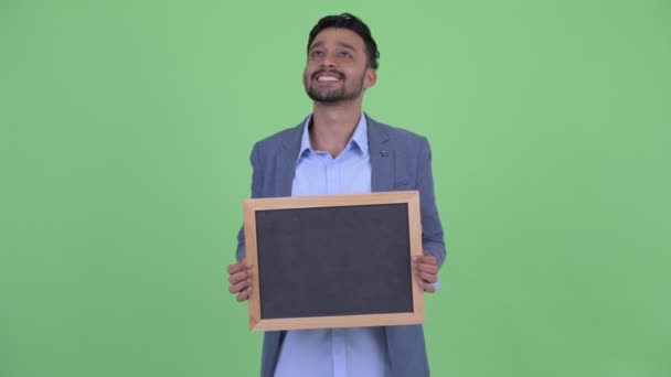 Boldog fiatal szakállas perzsa üzletember gondolkodás tartása közben tábla — Stock videók