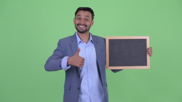 Happy young bearded Persian businessman holding blackboard and giving thumbs up — Stock Video