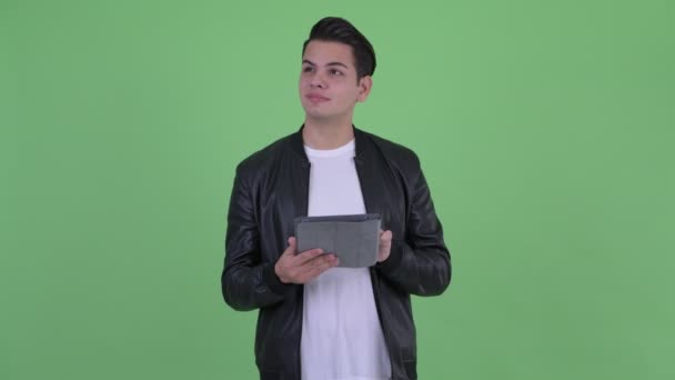 Счастливый молодой красивый многоэтничный мужчина думает, используя цифровой планшет — стоковое видео