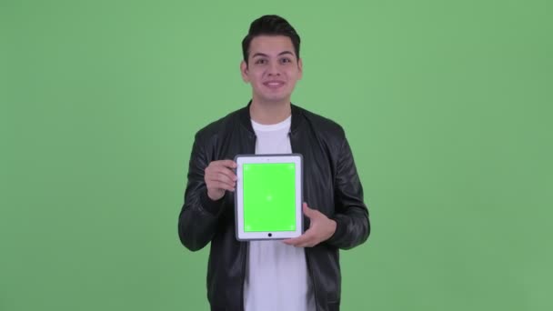 Glücklicher junger gutaussehender multiethnischer Mann zeigt digitales Tablet und sieht überrascht aus — Stockvideo
