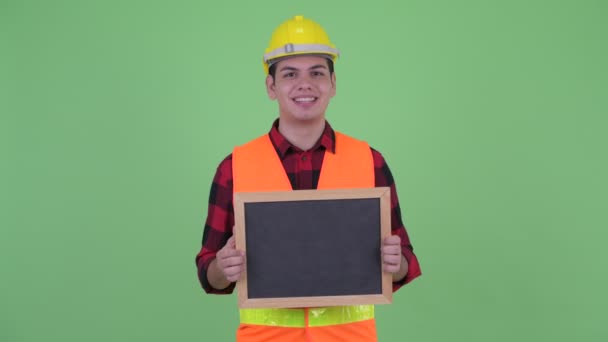 Fröhlicher junger multiethnischer Bauarbeiter spricht, während er die Tafel hält — Stockvideo