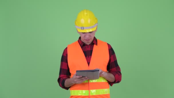 Glücklicher junger multiethnischer Bauarbeiter, der mit digitalem Tablet denkt — Stockvideo