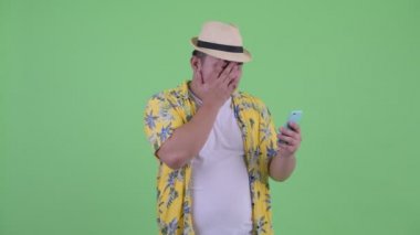 Stresli genç kilolu Asyalı turist adam telefon kullanarak ve kötü haber alıyorum