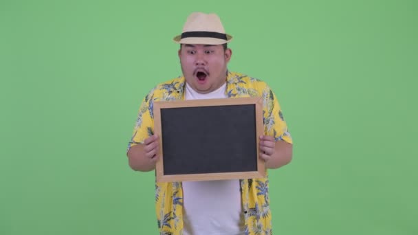 Šťastná mladá nadváha asijský turista držící tabuli a překvapený — Stock video
