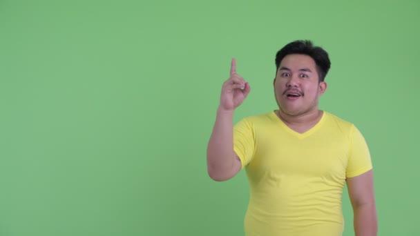 Lycklig ung övervikt asiatisk man pekar upp och ser förvånad — Stockvideo