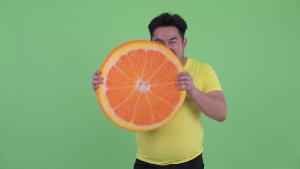 Счастливый молодой толстый азиат держит в руках оранжевую подушку как здоровую концепцию — стоковое видео