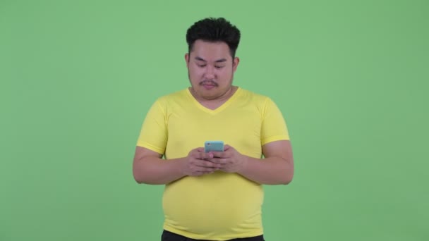 Šťastná mladá nadváha asijský muž uvažuje při používání telefonu — Stock video