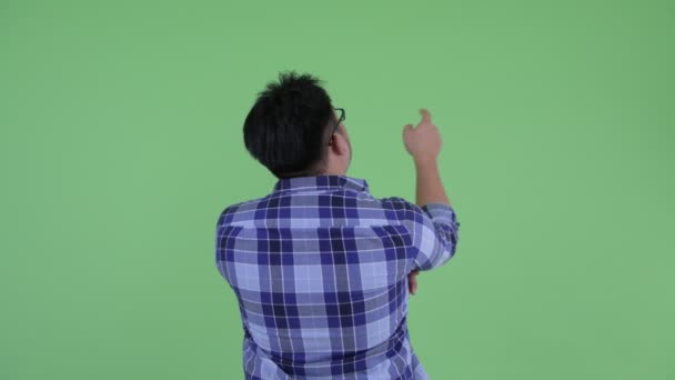 Zadní pohled na mladou nadváhu asijský hipsterman ukazující prstem a režie — Stock video