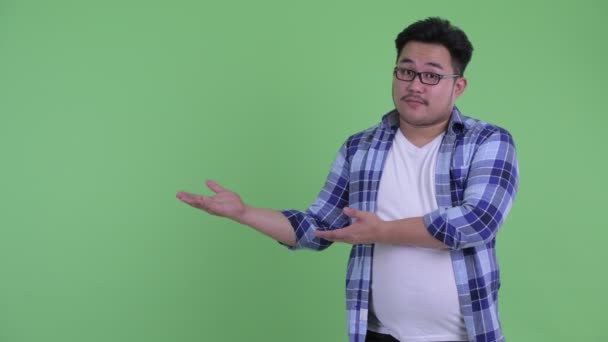 Happy young overweight Asian hipster man showing something and giving thumbs up — Stock Video