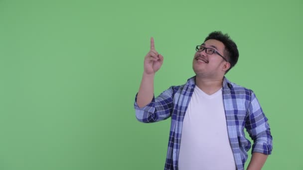 Happy young overweight Asian hipster man talking while pointing up — Stock Video