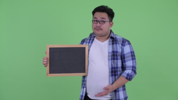 Benadrukte jonge overgewicht Aziatische hipster man Holding en het geven van duimen naar beneden — Stockvideo