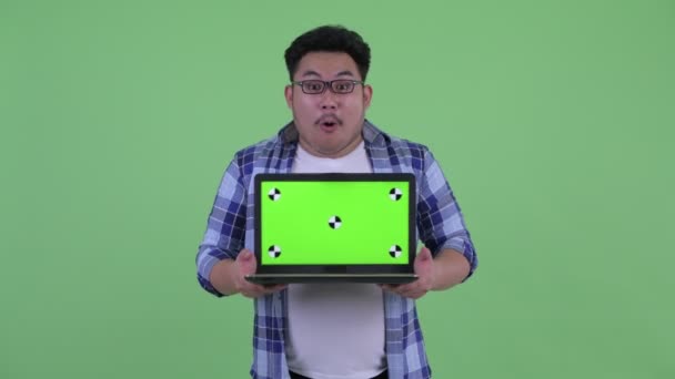 Boldog fiatal túlsúlyos ázsiai csípő ember mutatja laptop és látszó meglepett — Stock videók