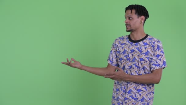 Glücklicher junger gutaussehender afrikanischer Mann spricht, während er etwas zeigt — Stockvideo
