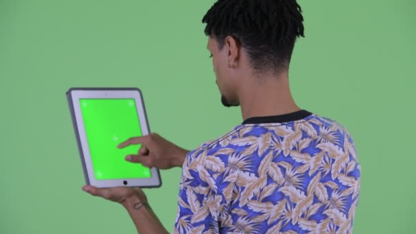 Rückansicht eines glücklichen jungen gutaussehenden Afrikaners mit digitalem Tablet — Stockvideo