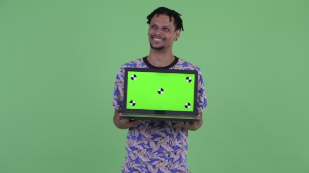 Happy young handsome African man thinking while showing laptop — Stock Video