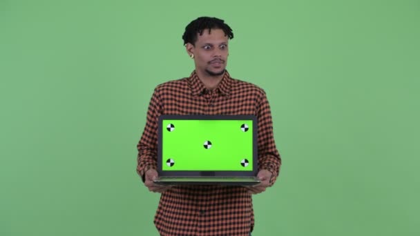 Happy young handsome African man talking while showing laptop — Stock Video