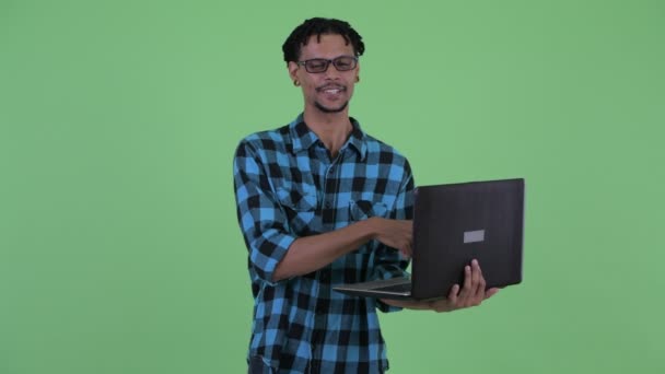 Ευτυχισμένος νέος Αφρικανός άντρας που μιλάει ενώ χρησιμοποιεί φορητό υπολογιστή — Αρχείο Βίντεο