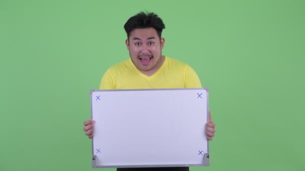 Happy young overweight Asian man holding white board — Stock Video