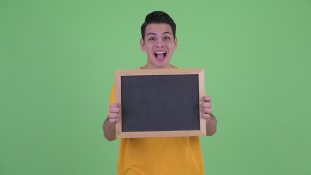 Glücklicher junger multiethnischer Mann hält Tafel und sieht überrascht aus — Stockvideo