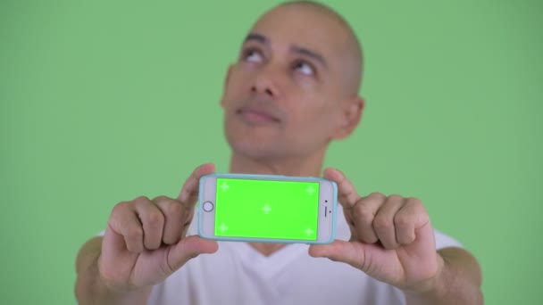 Gesicht eines gut aussehenden, glatzköpfigen Mannes, der beim Vorzeigen seines Telefons denkt — Stockvideo