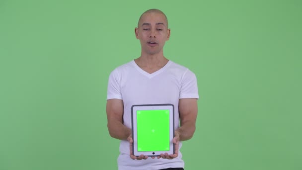 Veselý, hezký holohlavý muž, který mluví, když zobrazuje digitální tablet — Stock video