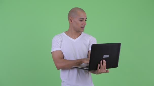 Happy handsome bald man thinking while using laptop — Stock Video