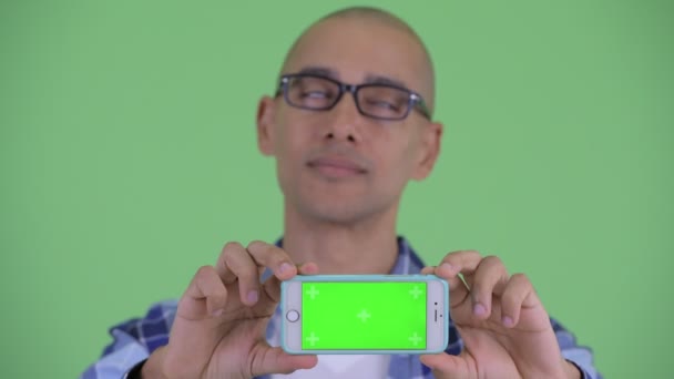 Obličej šťastného holohlavého hipstera, který si myslí, když se zobrazuje telefon — Stock video