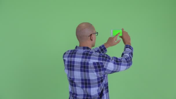 Rückansicht eines glatzköpfigen Hipsters, der mit dem Handy fotografiert — Stockvideo