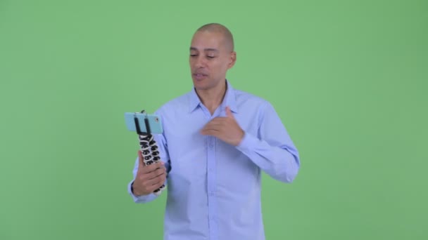 Šťastný holohlavý multietnický obchodník vkácení a zobrazující telefon — Stock video