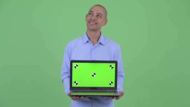 Happy bald multi ethnic businessman thinking and talking while showing laptop — Stock Video