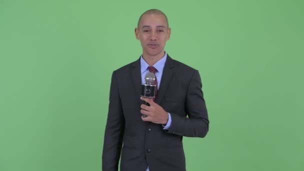 Happy bald multi ethnic businessman as host using microphone — Stock Video