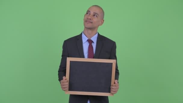 Happy bald multi ethnic businessman thinking while holding blackboard — Stock Video