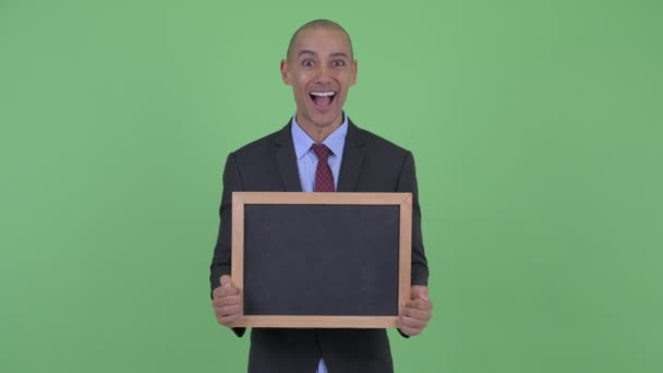 Happy bald multi ethnic businessman holding blackboard and looking surprised — Stock Video