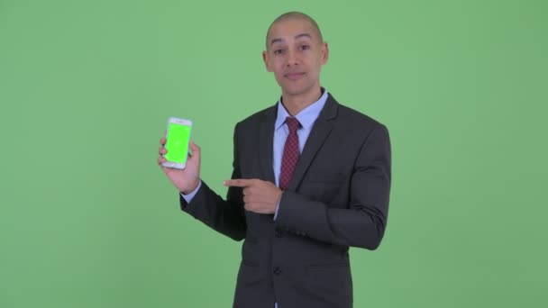 Щасливий лисий багатонаціональний бізнесмен показує телефон і дає великі пальці вгору — стокове відео