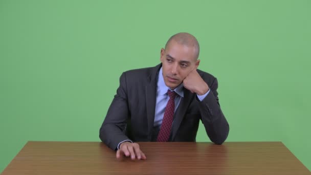 Stressed bald multi ethnic businessman looking bored and tired behind desk — Stock Video