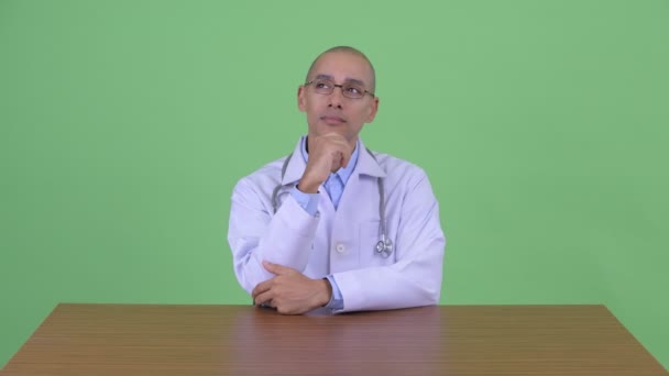 책상 뒤에 생각하는 행복한 대머리 다민족 남자 의사 — 비디오