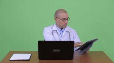 Meşgul kel çok etnik adam doktor masa arkasında iş yerinde multitasking