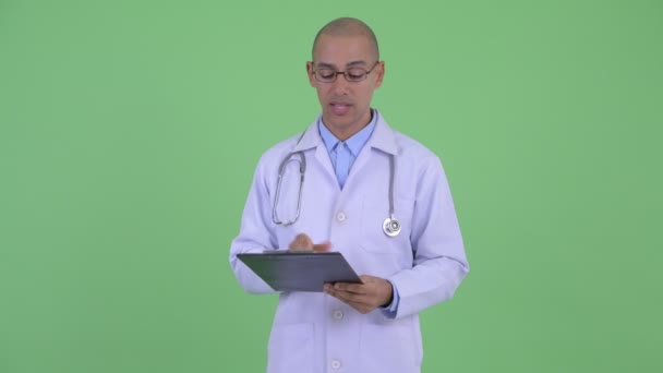 クリップボードを持ちながら話すハッピーハゲ多民族男性医師 — ストック動画