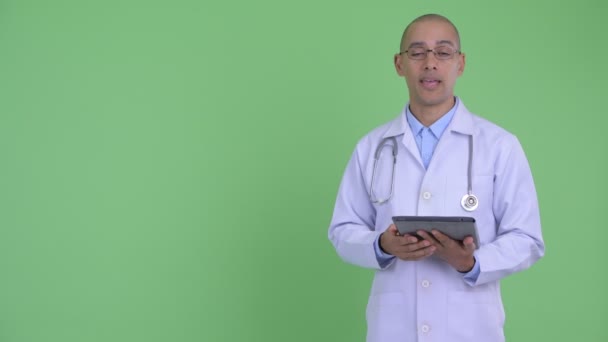 Happy bald multi ethnic man doctor talking and showing digital tablet — Stock Video