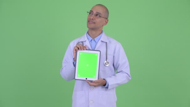 Feliz careca multi etnia homem médico pensando ao mostrar tablet digital — Vídeo de Stock